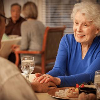 Elderly woman enjoying a meal and conversation at a restaurant.