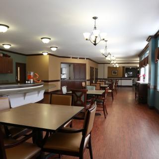 An empty dining area with neatly arranged tables and chairs, featuring warm lighting and wood flooring.