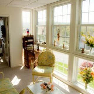 A sunny living room with large windows, floral decor, and cozy seating.