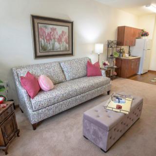 A cozy living room with a patterned sofa, colorful cushions, and a small kitchen in the background.
