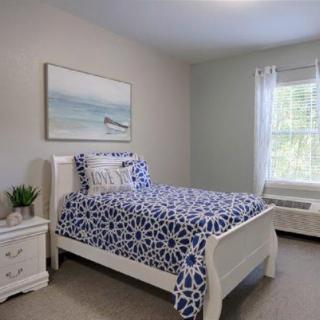 A cozy bedroom featuring a single bed with blue patterned bedding, white furniture, and natural light streaming through a window.