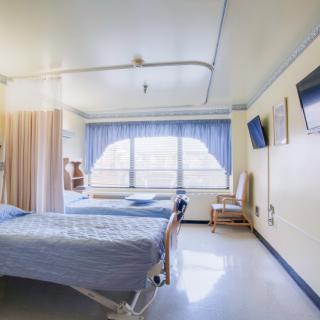 A clean and bright hospital room with two beds and a large window providing natural light.