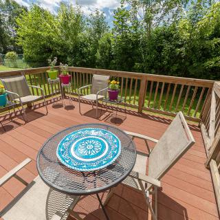 A sunny wooden deck with patio furniture and vibrant greenery in the background.