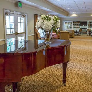 A grand piano adorned with a vase of flowers in a spacious, carpeted lobby.