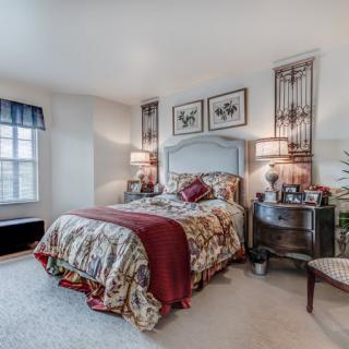A cozy, traditionally decorated bedroom featuring a bed with a floral comforter, nightstands with lamps, and artwork above the headboard.