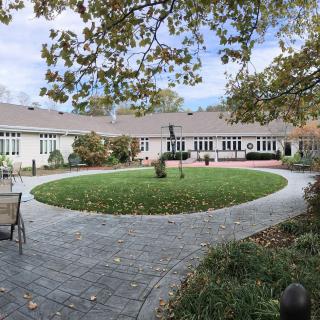 A serene courtyard with a circular grassy area surrounded by a paved pathway and a building in the background.