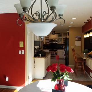 A cozy kitchen and dining area with a decorative chandelier, red walls, and a potted plant centerpiece.