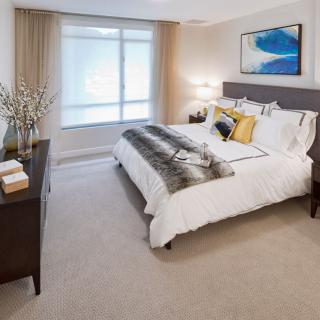 A modern bedroom with a large bed, decorated with neutral tones and vibrant artwork on the wall.