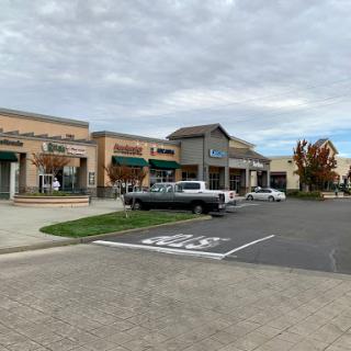 A view of a shopping center featuring various retail stores and a parking area under a cloudy sky.