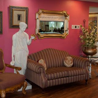 A stylish living room featuring a striped sofa, a classical statue, and decorative mirrors and artwork on a pink wall.
