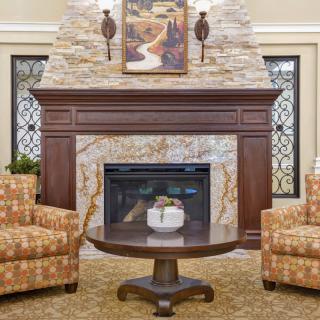 A cozy living room with a stone fireplace, flanked by two patterned armchairs and a round wooden coffee table.