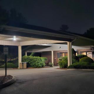A well-lit entrance of a building surrounded by lush greenery under the night sky.