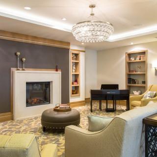 A cozy and elegant living room featuring a central fireplace, stylish chandelier, plush seating, and built-in bookshelves.