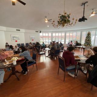 A group of people gathered in a well-decorated room with holiday decorations, sitting at tables and engaging in conversation.