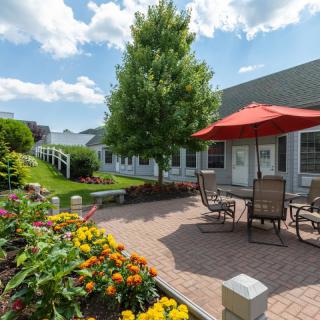 A charming garden patio with colorful flowers, outdoor seating, and a red umbrella on a sunny day.