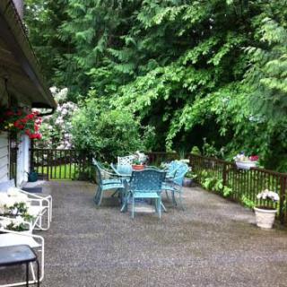 A serene outdoor patio area with chairs and a table surrounded by lush greenery.