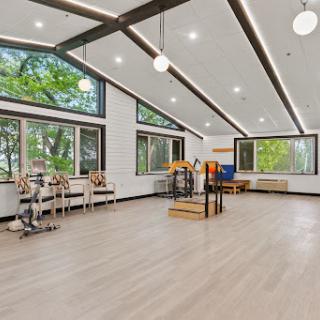 A bright and spacious fitness studio with large windows, wooden floors, and modern decor.