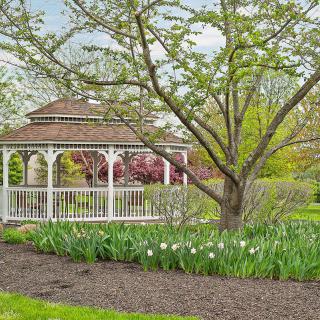 A serene garden scene featuring a white gazebo, surrounded by trees and blooming flowers.