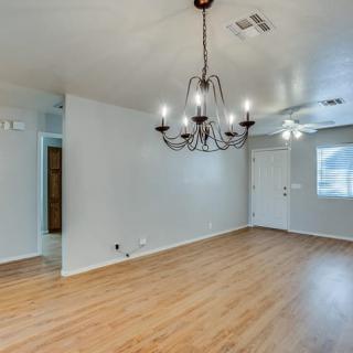 An empty living room with wood floors, a chandelier, and a ceiling fan.