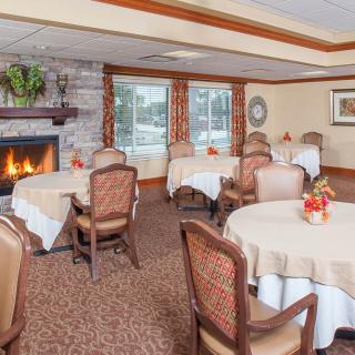 A cozy dining room with round tables and a fireplace, featuring elegant decor.