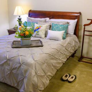 A cozy bedroom with a neatly made bed, adorned with decorative pillows and a tray of flowers.