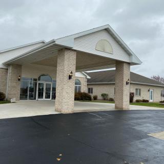 A modern building with a covered entrance and glass doors, set against a cloudy sky.