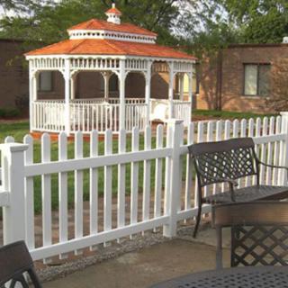 A peaceful outdoor area featuring a white gazebo, surrounded by a white picket fence and patio furniture.