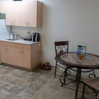 A small kitchenette with cabinets, a coffee maker, and a table with chairs.