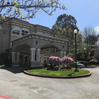 A large, elegant building surrounded by well-maintained gardens and trees on a sunny day.