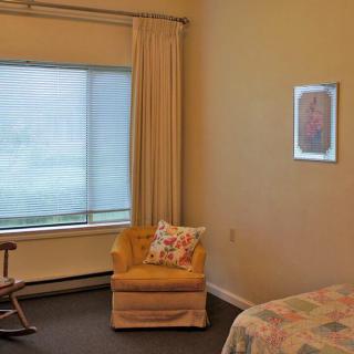 A cozy room with a large window, featuring a comfortable chair, curtains, and a bed.