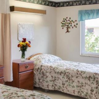 A cozy bedroom featuring two beds with floral bedding, a nightstand with a flower vase, and a bright window.