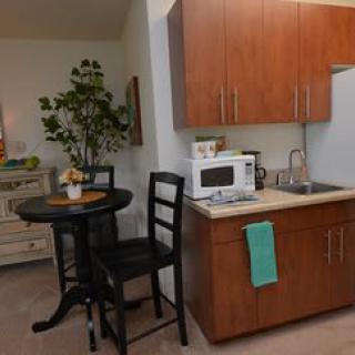 A compact kitchen and dining area with modern amenities, including a microwave, sink, and a small round table with chairs.