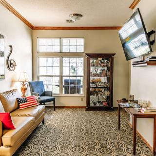 A cozy living room with a sofa, armchair, and TV, featuring decorative elements and ample natural light from a large window.