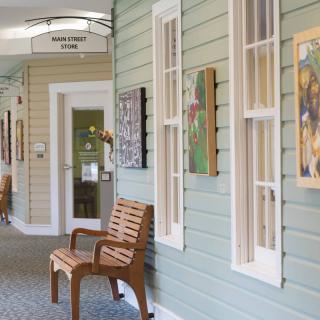 A brightly lit hallway with artwork displayed on the walls and a wooden bench positioned underneath.