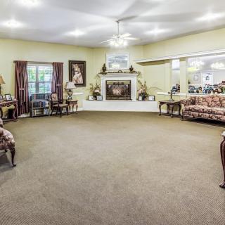 A spacious living room with carpeted floor, featuring sofas, a fireplace, and wall decor.