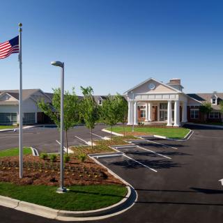 A view of a building with Greek-style columns, surrounded by a parking lot and an American flag under a clear blue sky.
