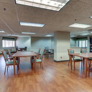 An empty dining hall with tables and chairs arranged on a wooden floor.
