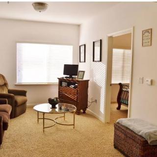 A cozy living room with a sofa, armchair, TV stand, and a coffee table near a large window.