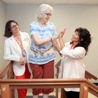 A patient receives support and encouragement from two healthcare professionals during a physical therapy session.