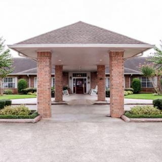 A building entrance with brick pillars and a covered walkway, surrounded by well-maintained landscaping.