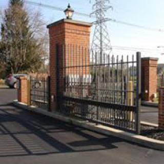 A metal gate with brick pillars and a lamp post, serving as an entrance.