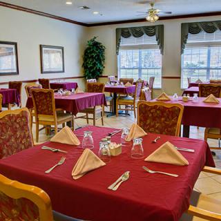 A neatly arranged dining area with tables set for a meal, featuring red tablecloths and cloth napkins.