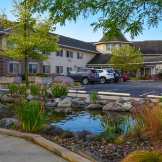 A charming residential facility surrounded by lush landscaping and a tranquil pond.