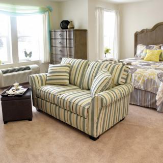 A cozy bedroom with a striped couch and bed, filled with natural light.
