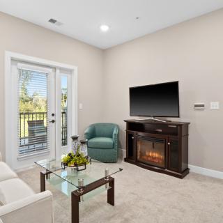 A modern living room featuring a fireplace with a television above it, a glass coffee table, and seating area with a sofa and armchair.