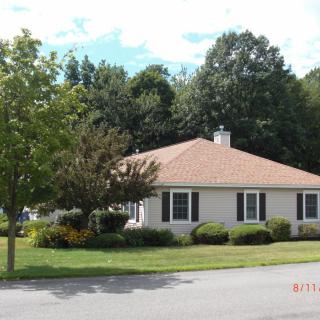 A suburban house with a well-maintained lawn and surrounding trees on a sunny day.