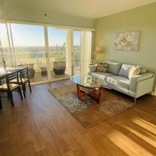 A bright and modern living room with a cozy seating area and dining space, featuring large windows that provide plenty of natural light.