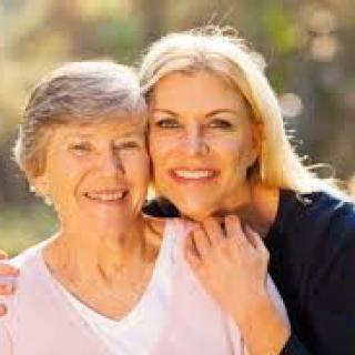 A younger woman embracing an older woman, both smiling outdoors.