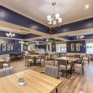 A spacious dining area with elegant chandeliers, featuring blue walls and wooden floors.