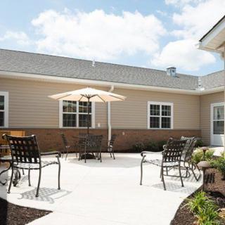 A sunny outdoor patio area with chairs, a table, and an umbrella next to a building.